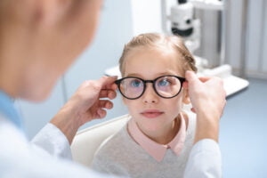 optometrist putting glasses on and a young girl