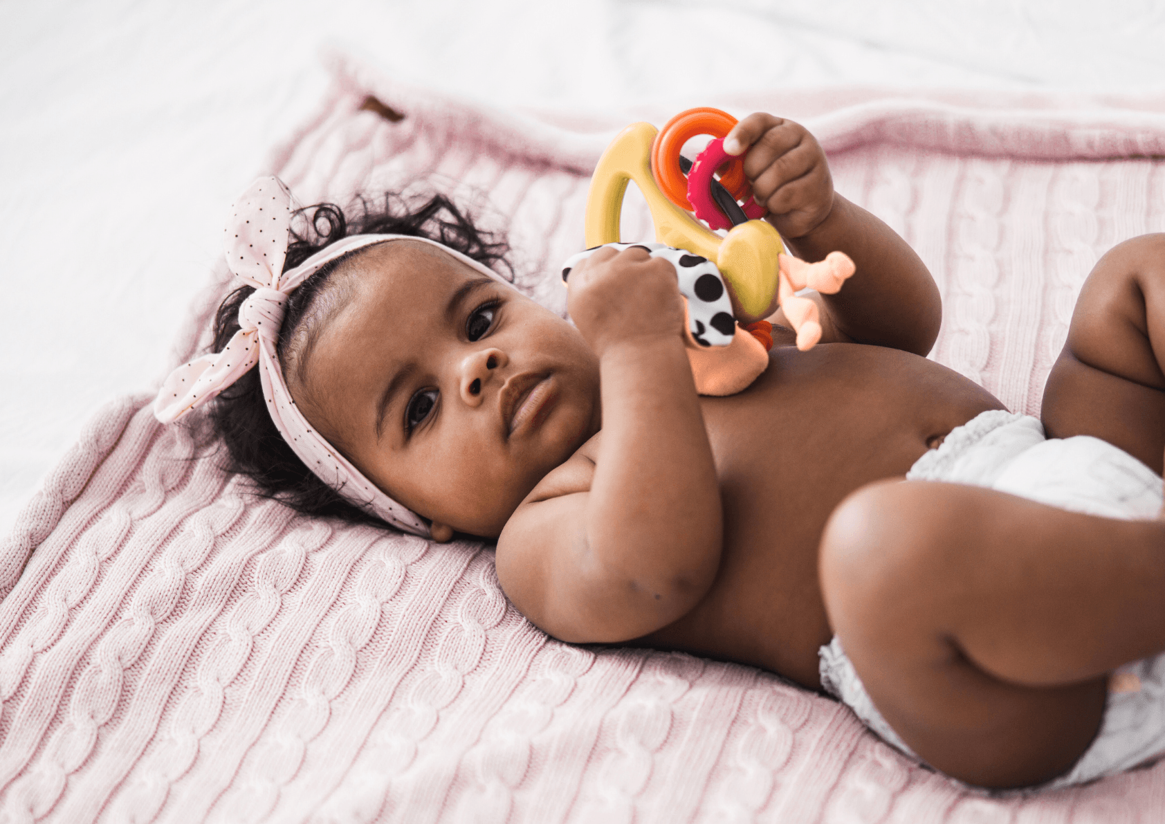 Baby holding toys on pink blanket while attending children's hospital
