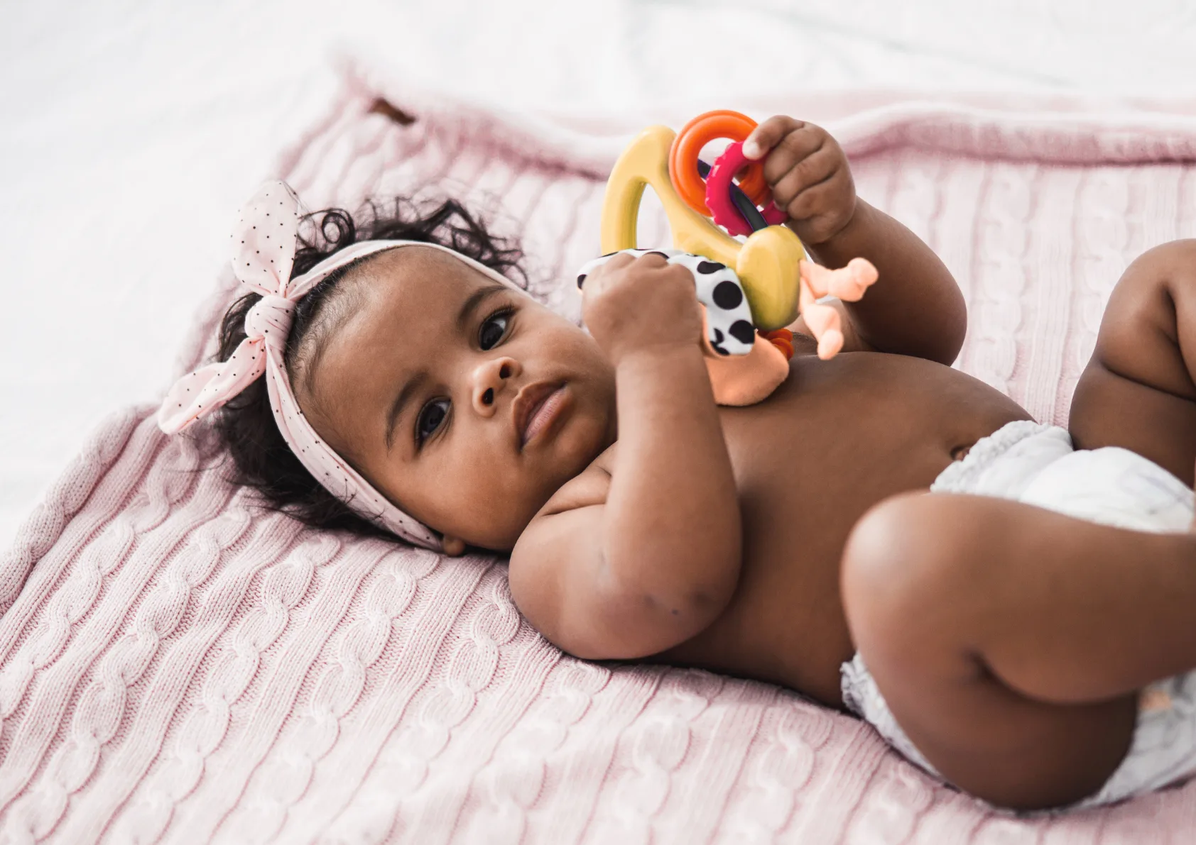 Baby holding toys on pink blanket while attending children's hospital