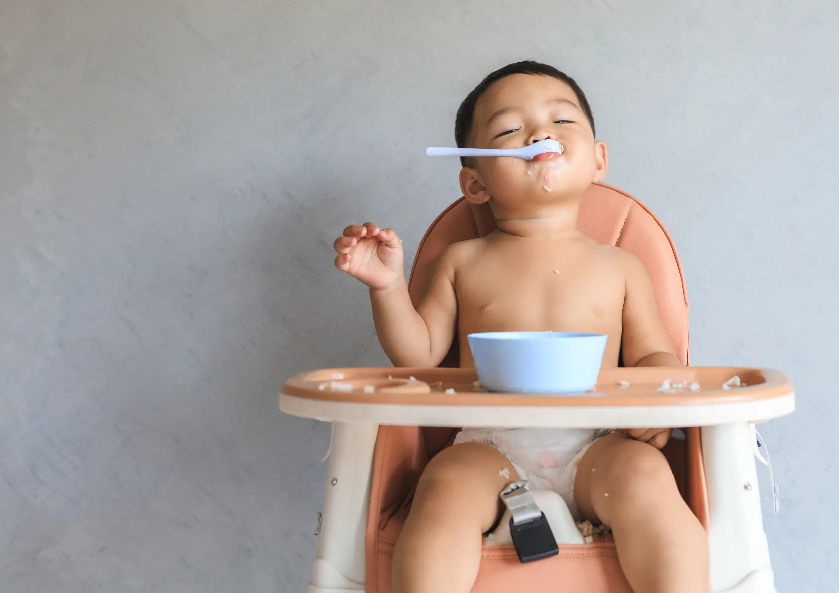 Baby boy sitting in high chair eating with spoon